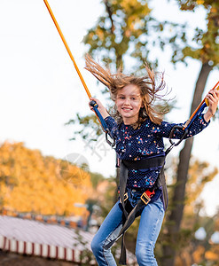 微笑的小女孩跳到蹦床上绳上乐趣女儿操场活动吸引力童年城市幸福闲暇娱乐图片