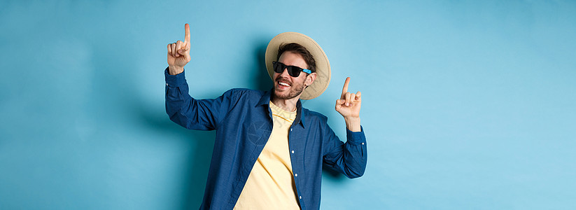 度假时的有趣的旅游舞蹈 举起手指 穿着夏帽和墨镜 蓝底脸色太阳镜帽子广告男人成功生活办公室快乐假期男性图片