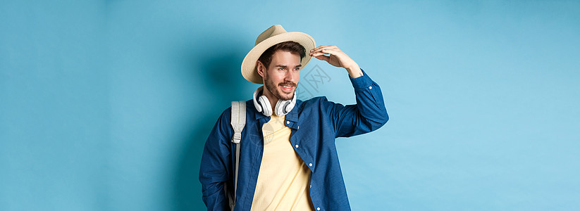 戴着草帽的帅气游客 遮住脸 看着远处 微笑着高兴 暑假旅行 站在蓝色背景上男人胡子胡须男性广告快乐工作室生活商业旅游图片