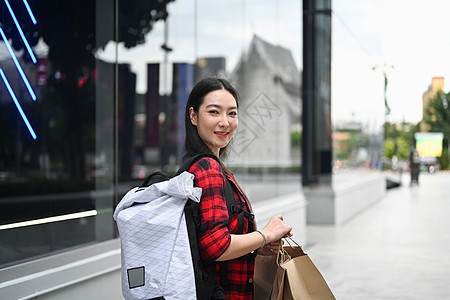 手持购物袋和在户外购物中心行走的年轻亚洲妇女微笑着图片