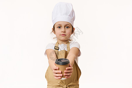 可爱的女婴 - 一个穿白色厨师帽子和美食围裙的小咖啡员 在生态纸杯里卖热饮图片