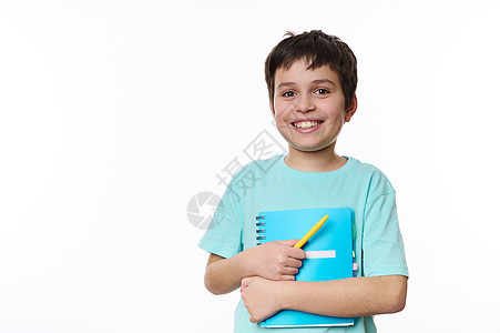 聪明的小学生 聪明的少年男孩 拿着教科书和黄笔 笑着C在相机上 白背景图片