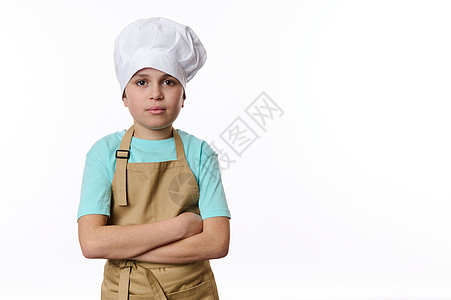 英俊的十几岁男孩装扮成面包师美食师 穿着厨帽和甜菜围裙 在白色上被孤立图片