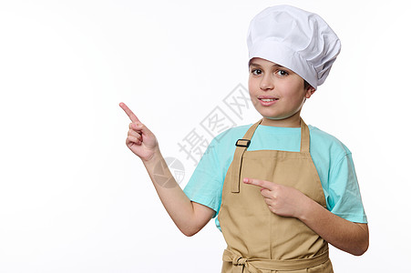穿着厨帽和围裙点的可爱十几岁男孩 在免费空间用白色背景宣传文字 看镜头图片