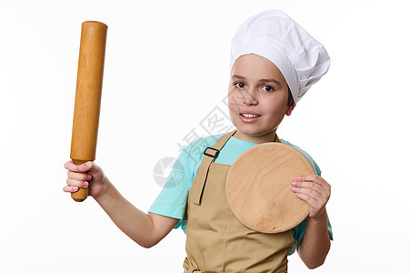 可爱的男孩 穿着厨师帽子和围裙 用滚针和木制剪板在白色背景上摆姿势图片