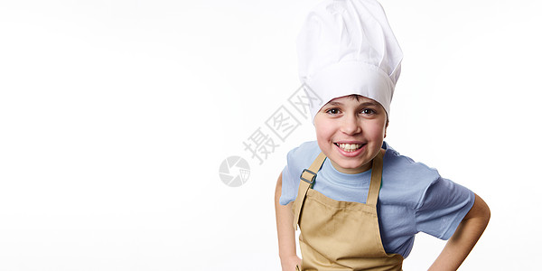 令人惊叹的男孩烹饪面包师 穿着白色厨帽和美甲围裙 手握腰带 对着摄影机笑笑图片