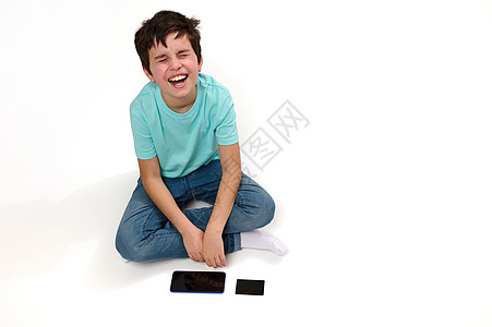 一位不满的高加索男孩最乐观的景象 带着智能手机和信用卡坐在白色背景的白种背景上表示悲伤图片