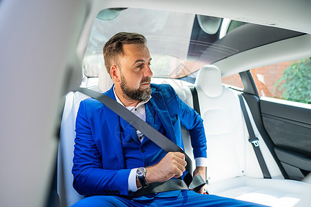 一个穿蓝西装的天主教男子在汽车后座系安全带 公务舱乘客 请坐商务窗户商业车辆胡子快乐套装座位管理人员享受图片