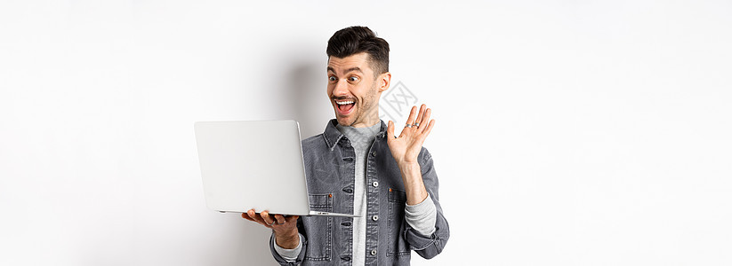 兴奋的男子在笔记本上放弃手 电脑上视频聊天 微笑友好 站在白色背景上商业情绪自由职业者技术快乐男人广告工作室办公室互联网图片
