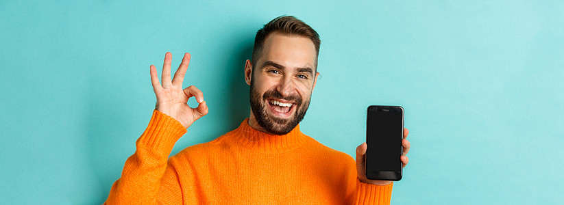 Caucasian男子照片显示移动屏幕及可使用签名 批准在线商店 智能手机应用程序 对浅蓝背景的满意度橙子工作室广告标识喜悦男人图片