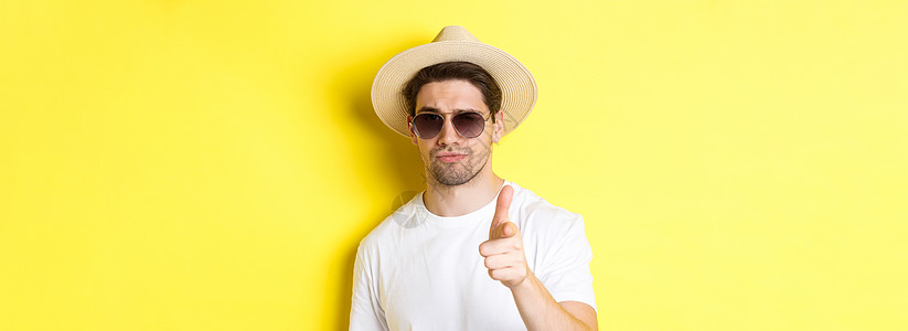 旅游和度假的概念 穿着夏日帽子和太阳镜的帅哥特写镜头指着相机 站在黄色背景上成人快乐潮人商业微笑旅行情绪手势假期广告图片