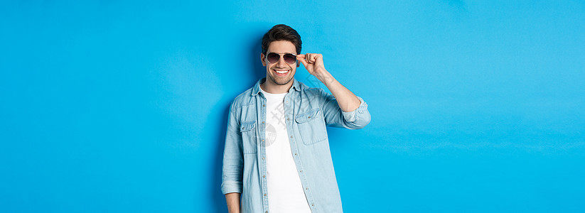 自信的男性男子汉戴上太阳眼镜 看上去很酷又自以为是 站在蓝背景上广告促销黑发潮人情绪快乐胡须成人胡子商业图片