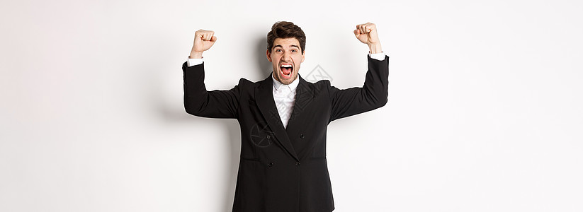 成功英俊的商务人士胜利 举起手来呼喊是的 欢庆成就 站在白种背景下站立起来雇主人士男人企业家老板经纪人房地产优胜者金融广告图片