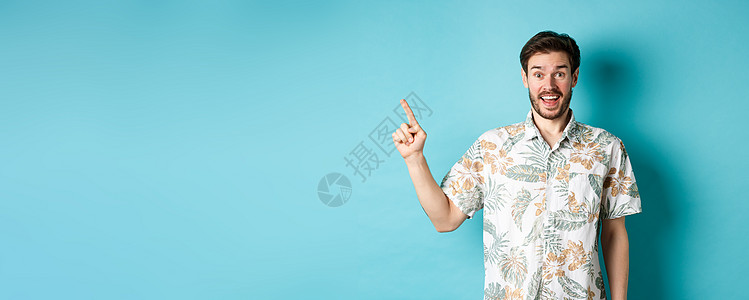 令人惊讶地欢喜的游客将手指指向空旷的空间 展示出酷的宣战者 穿着蓝色背景的浴衣站在哈瓦伊人衬衫上旅游成人广告男性生活商业胡子男人图片