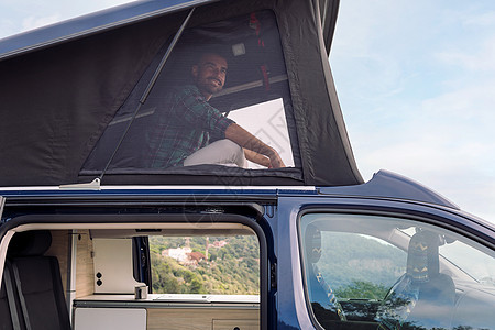 男人从面包车屋顶上看风景闲暇自由货车窗口帐篷成人旅行冒险快乐露营者图片
