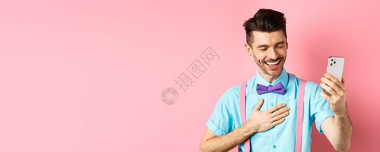 站在粉红色背景上的帅哥在视频聊天中大笑 进行移动对话并从一些有趣的事情中笑出声的形象微笑胡子成人办公室发型吊带裤工具胡须商业手机图片