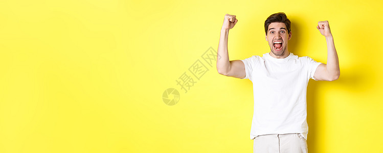 激动人心的男子获胜 举起手来庆祝 为团队赢得胜利和扎根 站在黄色背景之上的画面微笑商业成功广告成人快乐成就胡须情绪手势背景图片