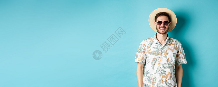 穿着太阳镜和暑假衬衫的帅帅笑男人 享受巡游假期 站在蓝背景上快乐生活旅游工作室帽子胡子广告旅行男性男人图片