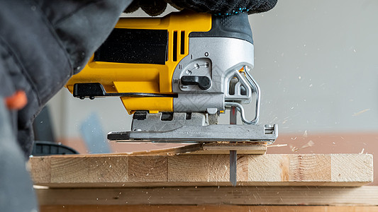 一名男子在车间用电锯砍木板的缝合装置上材料裁剪机器木头家具木材男性工匠锯末活动图片