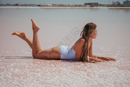 长头发的年轻女子在粉红色的咸水湖中 上面有盐晶体 含盐量极高的粉红色湖泊 因结晶盐沉积的微藻而染上颜色 水疗 美容和保健概念岩石图片
