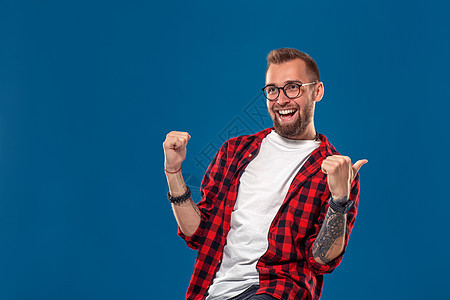 长着笑脸的年轻大胡子男子 穿着一格衬衫 用手指显示方向;在蓝色背景上孤立无援图片