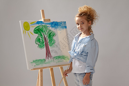 迷人的女学生正在用水彩刷画在壁架上 站在灰色背景上生活画家学习蓝色艺术品孩子们衬衫艺术家女孩调色板图片