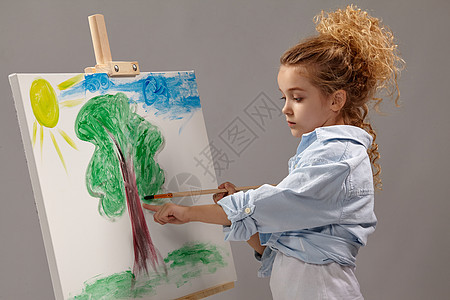 迷人的女学生正在用水彩刷画在壁架上 站在灰色背景上创造力艺术家乐趣绘画学校发型画笔生活画架刷子图片