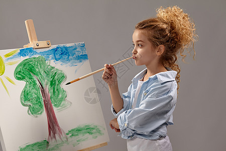 迷人的女学生正在用水彩刷画在壁架上 站在灰色背景上艺术品学习创造力绘画艺术家享受画笔调色板太阳工艺图片