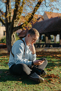 专业摄影师拍摄美丽的秋天公园 男子专业摄影师坐在秋天公园的相机和智能手机 润饰 鲜艳的色彩 褐色调公园成人男性森林男人照片镜片单图片