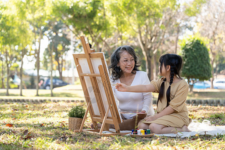 快乐可爱的亚洲祖母教孙女在画布上画水彩 在美丽的公园里度过了愉快的时光成人女孩花园女性女儿微笑孙子祖父母亲童年图片