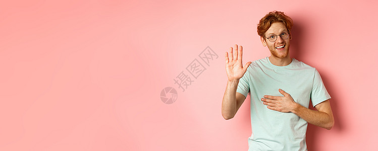 友善的红头发男人很诚实 手牵着心 高高举起手臂发誓或许下诺言 对着镜头微笑 在粉红色背景下说实话胡须广告成人学生男性红色发型粉色图片