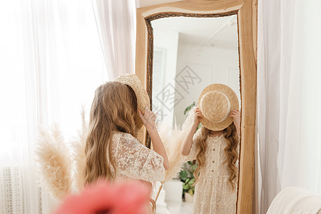 长发的美少女在镜子前戴上草帽 对金发女郎的自以为是的感觉拥抱达人稻草风格女士洞察力青少年衣服身体装饰图片