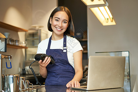 微笑的亚洲咖啡师 带卡终端 支付机和笔记本电脑的女孩 站在咖啡馆里 处理咖啡订单的付款食物职场商务人士食堂员工女性工人职业服务图片