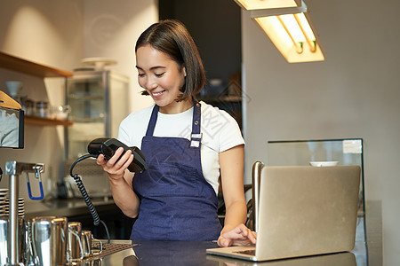 微笑的亚洲咖啡师使用卡片机处理客户付款 客人在咖啡店支付订单图片