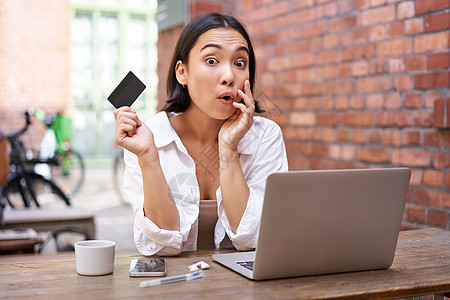 时尚的亚洲年轻女性在网上购物 拿着信用卡和笔记本电脑坐着 在网上购物 非接触式支付 处理账单帐户商业技术黑发互联网自由职业者银行图片