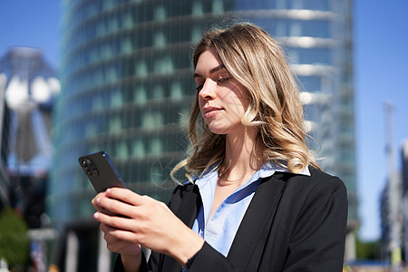 面试邀请在城市街道上使用手机的自信企业女性的画像 女商务人士站在户外时通过智能手机应用程序发送消息城市面试商务雇主金融人士女士员工职场企背景