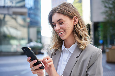 年轻女商务人士在户外站立时使用移动电话 微笑着年轻的商业妇女 公司人的概念图片
