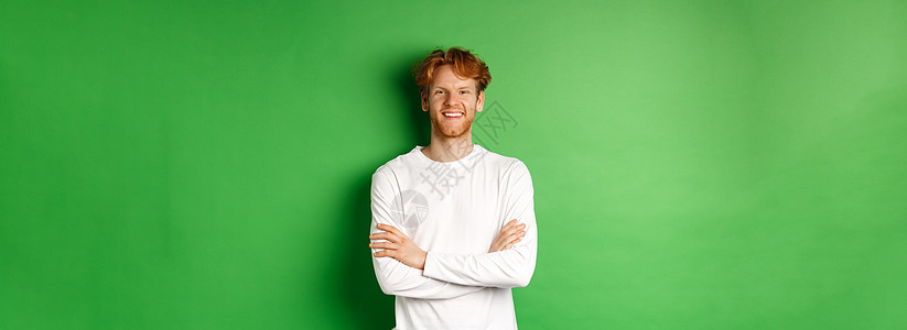 雄心勃勃的年轻男子 红发站在绿色背景上 手牵着胸口 微笑红色成人发型学生购物潮人男性广告冒充工作室图片