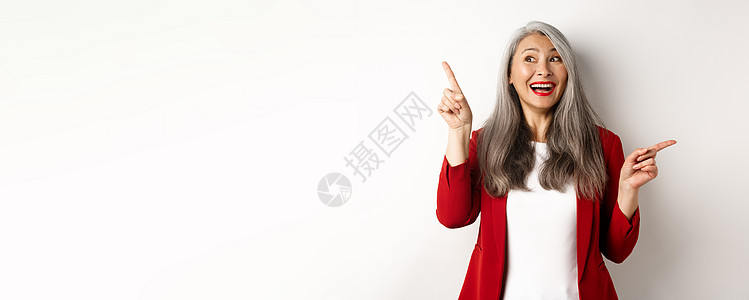 笑得开心的亚洲女士微笑 用手指对着两张促销报价 站在白色背景上穿着红衣快乐地站立工人人士套装商务技术企业家化妆品成人工作经理图片
