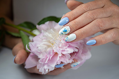 有美丽的白蓝色美甲的女孩 带着一束精细的花朵指甲温泉女性化妆品治疗美容女士抛光手臂沙龙图片