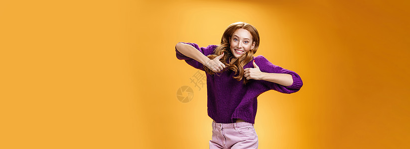 乐观快乐的鲜姜女孩开心地跳着 开心地竖起大拇指 赞同并在橙色墙上对超酷的想法或概念给予积极反馈成人发型毛衣学生欢呼女性压痛紫色投图片
