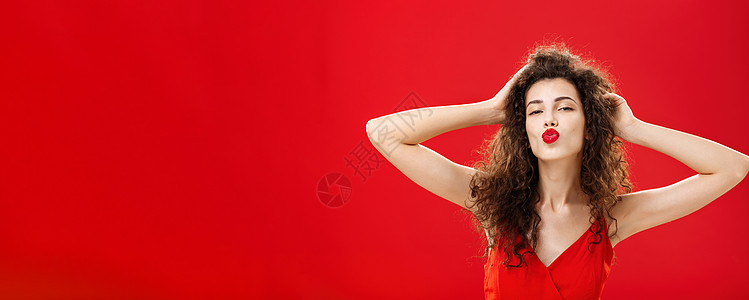 自信轻浮 优雅的年轻富有女性的腰部照片 她的头发卷曲 穿着红色的唇膏和晚礼服 在 mwah 中抚摸着头发折叠的嘴唇 亲吻着仰慕者图片