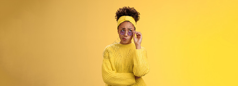 戴着头带毛衣太阳镜的时尚非洲裔美国女性创意设计师困惑不解地笑着折叠嘴唇管不确定有疑问皱着眉头抬头深思熟虑无法决定大学员工护理印象图片