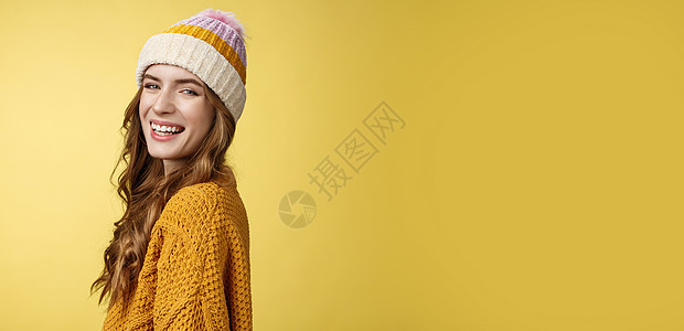 侧面拍摄迷人无忧无虑的快乐微笑女孩转动相机快乐地笑着享受寒假滑雪的乐趣 戴着帽子针织毛衣黄色背景笑着站着欢呼派对温暖女性名声成人图片