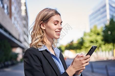 公司妇女站在街上和手机短信上 在看着智能电话屏幕时微笑着笑容的身影金融办公室套装营销面试工作雇主自信街道员工图片