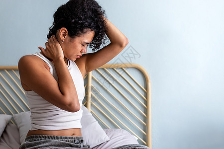 年轻的多种族拉蒂纳妇女坐在床上脖子疼痛 醒来时患有宫颈不适症的女子图片
