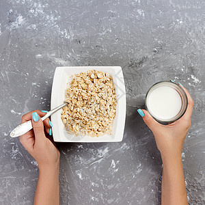 女孩用牛奶把它倒进燕麦 以灰色背景 顶尖的眼光提供有用和健康的早餐图片