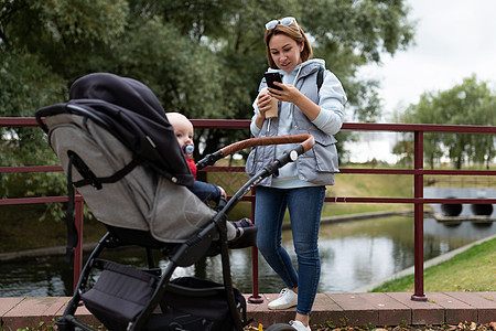 年轻母亲带着婴儿婴儿车在公园散步 手拿着电话的少女母亲图片