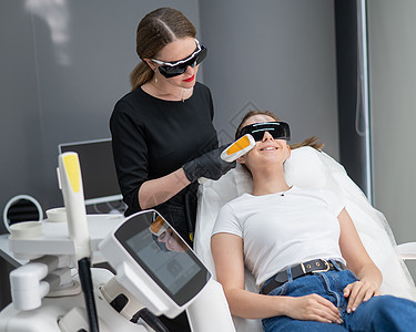 一个穿着护目镜的沙发上的女人 正在经历一个光复过程 硬体美容学诊所病人理疗粉刺女性温泉皮肤科仪器老化频率图片