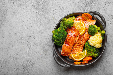 健康的烤鱼鲑鱼排 西兰花 花椰菜 胡萝卜在灰色石头背景的黑色铸铁砂锅碗中 烹调可口低碳水化合物晚餐 健康营养 文本的空间烤箱菜单图片